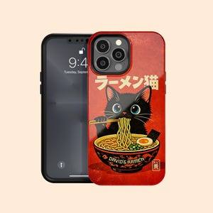 Puede incluir: Funda de teléfono roja con un gato negro de dibujos animados comiendo ramen. El cuenco de ramen tiene el texto "DAVID'S RAMEN". Texto japonés en la parte superior. El gato tiene ojos azules. Hay un teléfono negro al lado.