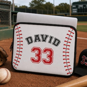 Puede incluir: Una funda rectangular blanca para portátil con un diseño de béisbol y patrones de costura rojos en los laterales. El centro muestra el nombre DAVID en letras negras sobre el número 33 grande en rojo con un borde blanco y negro.