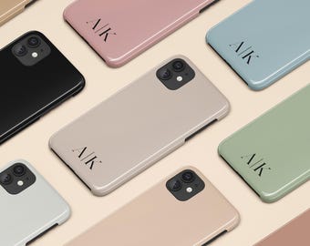 May include: A collection of smartphone cases in various solid colors including black, dusty rose, sage green, beige, and light blue. Each case features a dual-lens camera cutout and the black printed text A/K positioned near the bottom center.