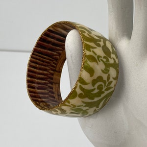 May include: A wide, green and white patterned bangle bracelet with a gold glitter trim.