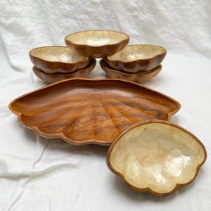 May include: A set of wooden serving bowls and a large leaf-shaped platter. The bowls have a light-colored interior and a dark brown exterior. The platter is a rich brown color, and the set is arranged on a white surface.