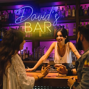 May include: A neon sign with the text "David's Bar" in blue and yellow letters. The sign is hanging above a bar counter with three people standing around it. Two people are holding glasses of beer and wine.