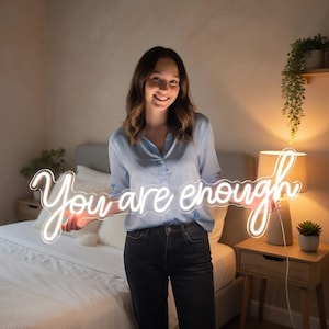 May include: A white neon sign featuring the cursive text "You are enough" illuminated with a bright glow. The sign is constructed with flexible tubing and is held horizontally, displaying the motivational phrase in a continuous, flowing script style.