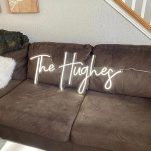 May include: White neon sign with the text "The Hughes" on a brown couch.