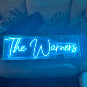 May include: A blue neon sign with the text "The Warners" in white neon lettering.