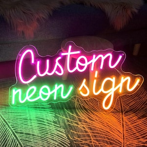 May include: A neon sign with the words "Custom neon sign" in pink, green, and orange. The sign is made of glass and has a clear background.