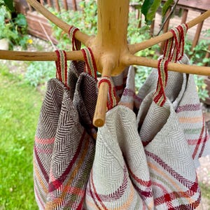 Könnte beinhalten: Ein hölzerner Handtuchhalter zeigt mehrere gefaltete Handtücher mit Fischgrätmuster. Die Handtücher haben rote, orange und grüne Streifen. Der Ständer ist aus hellem Holz und befindet sich im Freien.