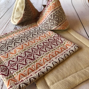 Könnte beinhalten: Set aus drei Topflappen aus braunem, orangefarbenem und cremefarbenem Stoff mit Mustern. Zwei sind dreieckig und einer ist rechteckig. Der rechteckige Topflappen hat eine einfache cremefarbene Stoffrückseite.