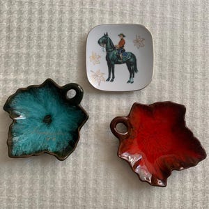 May include: Three decorative dishes are shown. A square dish with a horse and rider, and two leaf-shaped dishes, one teal and one red, with handles. These dishes are likely for serving small items, such as snacks or condiments.