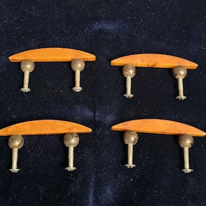 Peut inclure: Quatre poignées de meubles vintage. Chaque poignée présente une poignée incurvée de couleur orange soutenue par deux montants argentés en forme de boule avec des vis. Les poignées sont disposées sur un fond bleu foncé.