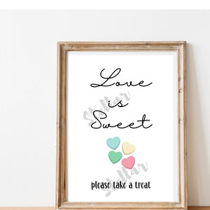 Puede incluir: Una impresión enmarcada con el texto "Love is Sweet" en fuente cursiva negra. Hay cinco corazones de caramelo de color pastel debajo del texto. El texto "please take a treat" está debajo de los corazones.