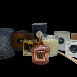 May include: An assortment of scented candles and diffusers in various glass containers. The candles are in clear glass with a textured design and the diffusers are in clear glass with a wooden lid. The candles and diffusers are all labelled with the word "KUDART".