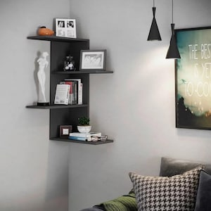 May include: A dark grey corner shelf unit with several shelves, displaying ornaments such as a statue, framed photos, books, and a small potted plant. The shelves are mounted on a light grey wall.