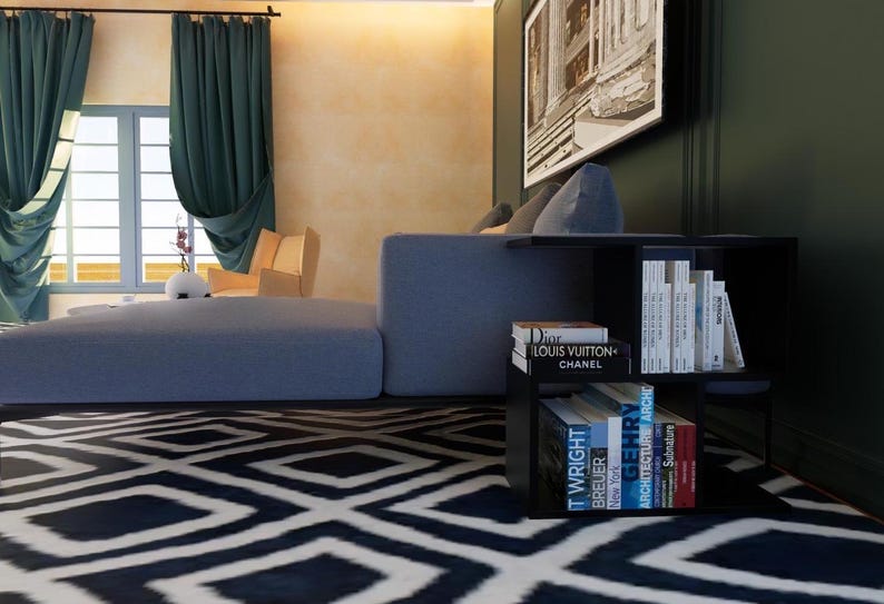 May include: A black side table with four shelves, holding a stack of books. The books have titles like "Dior", "Louis Vuitton", "Chanel", "T. Wright", "Breuer", "New York", "Architecture", "Century", and "Spectrum".