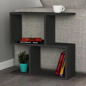 May include: Black side table with open shelves, featuring a book titled "Creative Illustration by Andrew Loomis" and another book titled "History of the Greatest Places" by Richard Bock. A small potted plant sits on the bottom shelf.