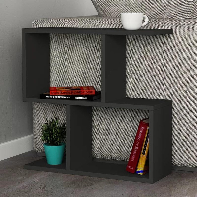 May include: Black side table with open shelves, featuring a book titled "Creative Illustration by Andrew Loomis" and another book titled "History of the Greatest Places" by Richard Bock. A small potted plant sits on the bottom shelf.