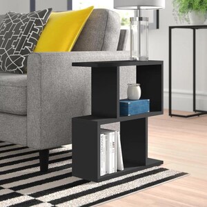 May include: Black side table with three shelves. The top shelf has a clear glass lamp with a silver base. The middle shelf has a blue box and a white candle. The bottom shelf has a stack of books with titles like "Art" and "Windows".