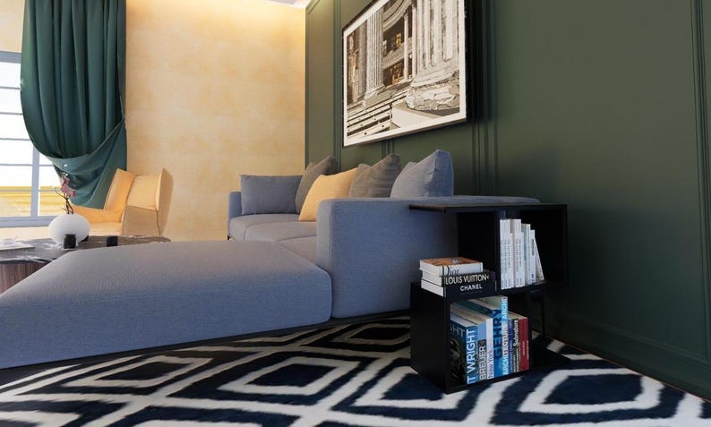 May include: A blue sectional sofa with a black metal frame sits in a living room with a black end table. The end table has three shelves filled with books, including one with the text "Louis Vuitton Chanel".