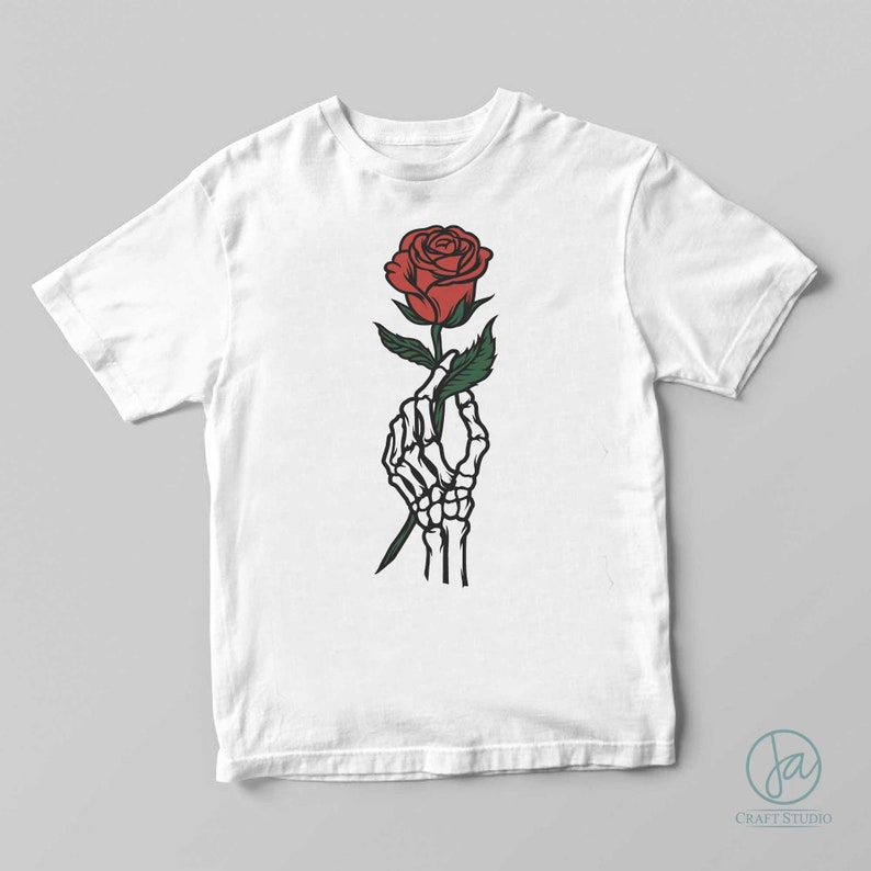 May include: A white t-shirt with a graphic of a skeleton hand holding a red rose.