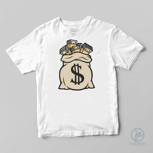 Op de afbeelding: Wit t-shirt met een cartoon illustratie van een beige geldbuidel met een groot zwart dollarteken. De tas stroomt over van stapels goudkleurig geld. Het ontwerp is gecentreerd op het shirt.