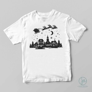 May include: A white t-shirt with a black silhouette design of Santa Claus flying over a small town with a church and houses. The design includes a crescent moon and stars.