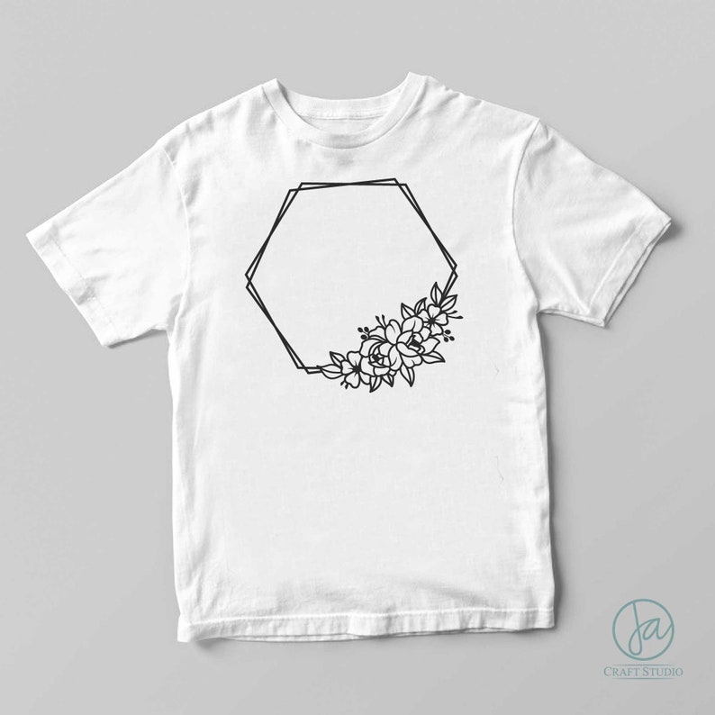 以下が含まれることがあります： 黒い幾何学的なフレームと花のデザインが施された白いTシャツ。フレームは六角形で、右下の角に花が集まっている。