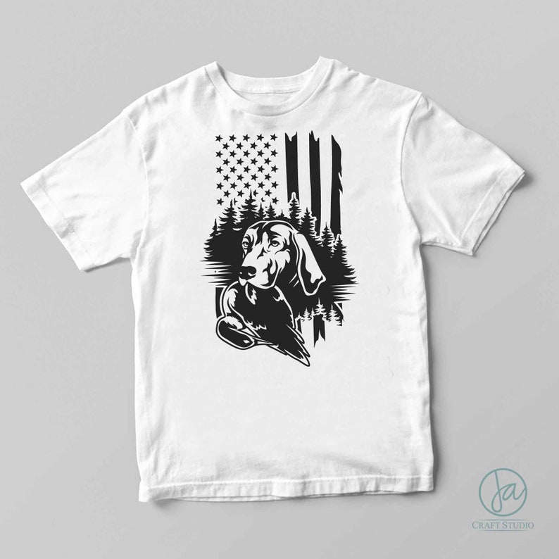May include: A white t-shirt with a black and white graphic of a dog holding a duck in front of an American flag.