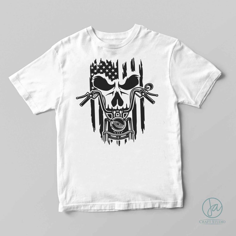 May include: A white t-shirt with a black and white graphic of a skull riding a motorcycle. The motorcycle is superimposed over an American flag.