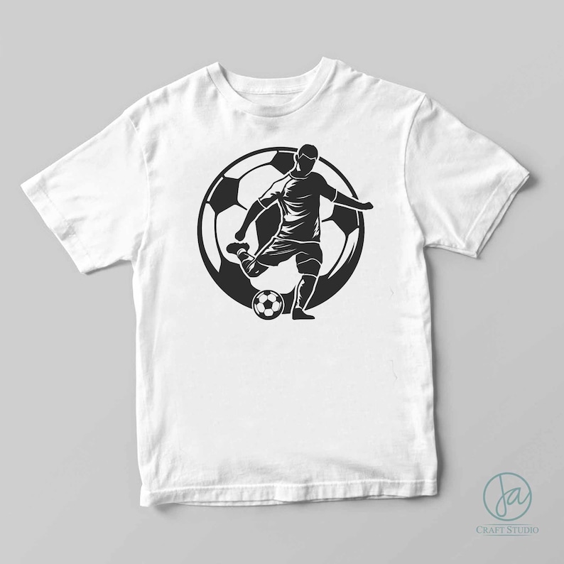 May include: A white t-shirt with a black silhouette of a soccer player kicking a ball. The player is surrounded by a large soccer ball.