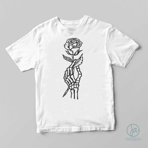 May include: A white t-shirt with a black line drawing of a skeleton hand holding a rose.