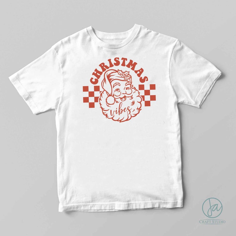 May include: White t-shirt with a red graphic of Santa Claus with the text "Christmas vibes" in a retro style.