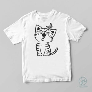 May include: White t-shirt with a black and white cartoon illustration of a cat with a butterfly above it.