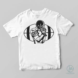 May include: White t-shirt with a black and white graphic of an American football player in a helmet, with the number 00 on the jersey. The player is in front of a football shape.