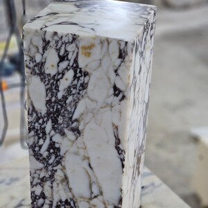 May include: A white marble block with brown and gray veining. The block is rectangular and has a smooth, polished surface.