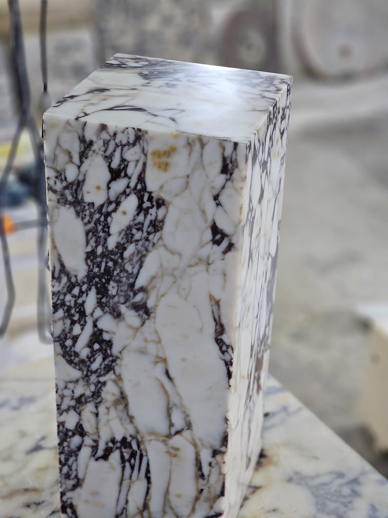 May include: A white marble block with brown and gray veining. The block is rectangular and has a smooth, polished surface.