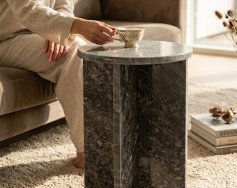 May include: A cylindrical side table crafted from dark grey marble with a polished finish, featuring a circular top supported by a cross-shaped base. The table has a smooth, speckled stone texture and a sturdy, vertical structure.