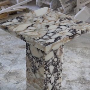 May include: A white marble table with a square top and a single pedestal base. The marble has brown and gold veins.