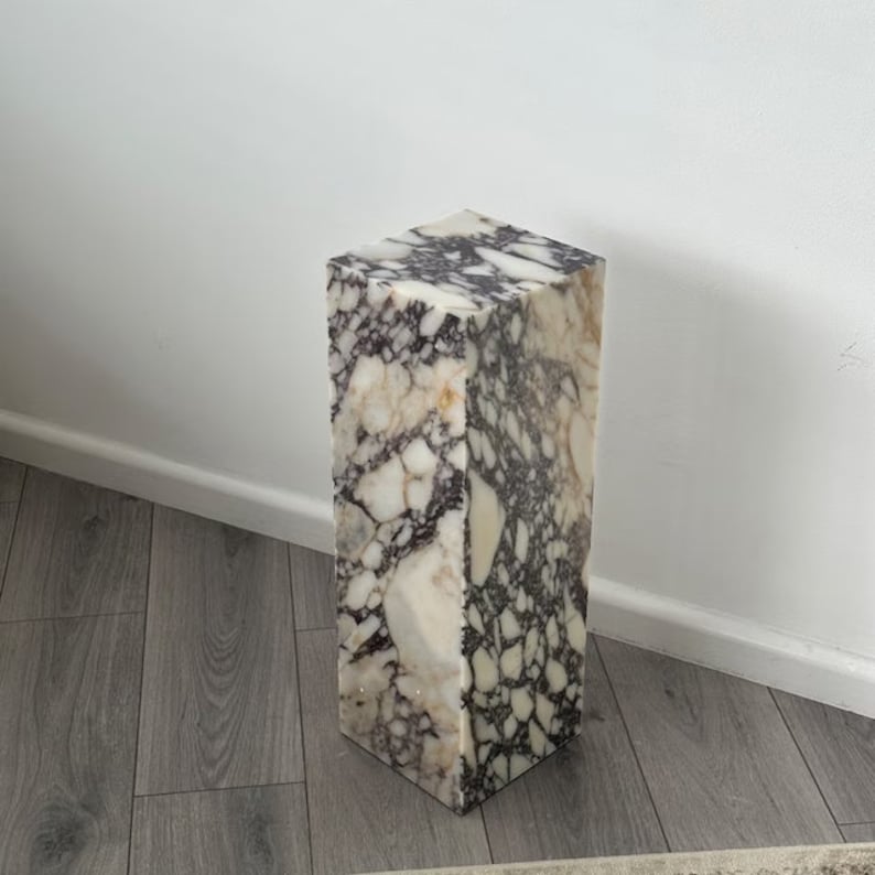 May include: A tall, rectangular marble pedestal with a white and purple marbled pattern. The pedestal is made of natural stone and has a smooth, polished finish.