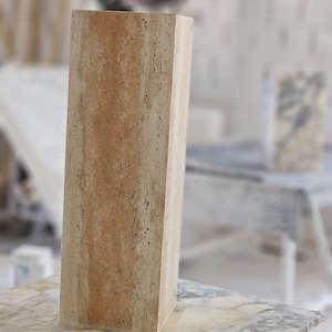 May include: A rectangular block of travertine stone with a light brown and beige color pattern. The stone is sitting on a marble surface.