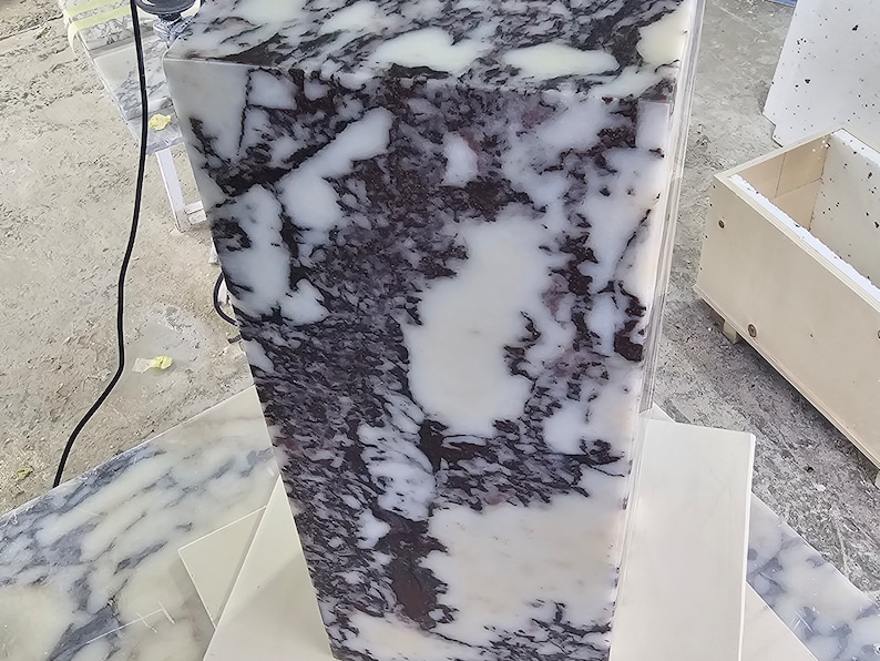 May include: A large, white marble block with purple and black veining. The block is sitting on a white surface.