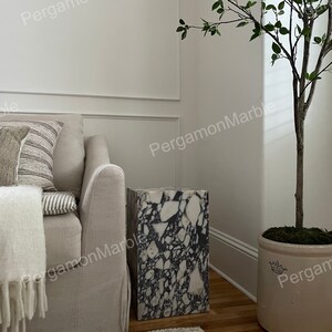 K&ouml;nnte beinhalten: Ein wei&szlig;er und schwarzer Terrazzo-Beistelltisch mit einem wei&szlig;en Sofa und einer Topfpflanze im Hintergrund.