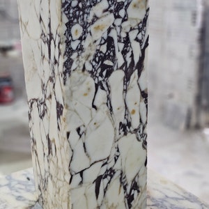 May include: A white marble block with black and brown veining. The marble has a polished finish and is rectangular in shape.