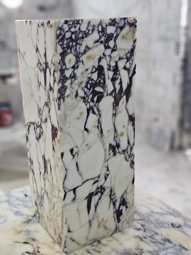 May include: A white marble block with black and brown veining. The marble has a polished finish and is rectangular in shape.