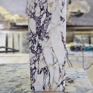 May include: A white marble slab with purple and brown veining. The slab is smooth and polished.