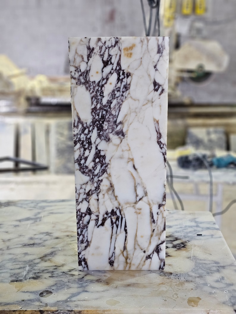 May include: A white marble slab with purple and brown veining. The slab is smooth and polished.