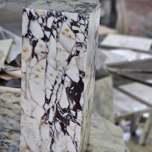 May include: A white marble block with brown and black veining. The block is rectangular and has a smooth, polished surface.