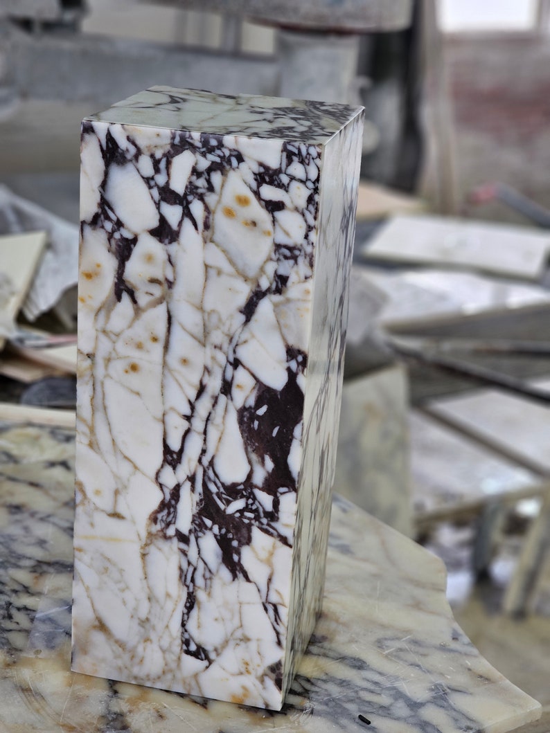 May include: A white marble block with brown and black veining. The block is rectangular and has a smooth, polished surface.