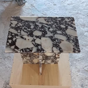 May include: A white marble table top with black and purple veining. The table top is sitting on a wooden base.