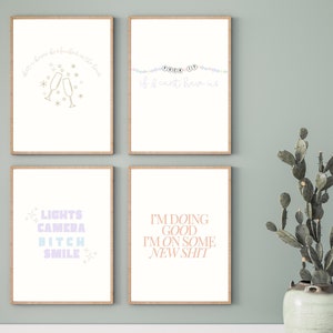 May include: Four framed prints with motivational quotes. The top left print features a champagne toast with the text "Just here for the good times". The top right print features a string of colorful beads with the text "F*ck it if I can't have us". The bottom left print features the text "Lights Camera Bitch Smile" in pastel colors. The bottom right print features the text "I'm doing good I'm on some new shit" in peach colored text.