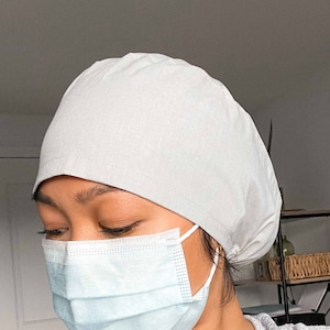 May include: A person wearing a light grey surgical cap and a light blue surgical mask. The person is wearing a grey heather shirt.